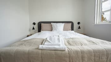 A neatly made bed with a beige comforter and pillows, a white towel, and two bedside lamps.
