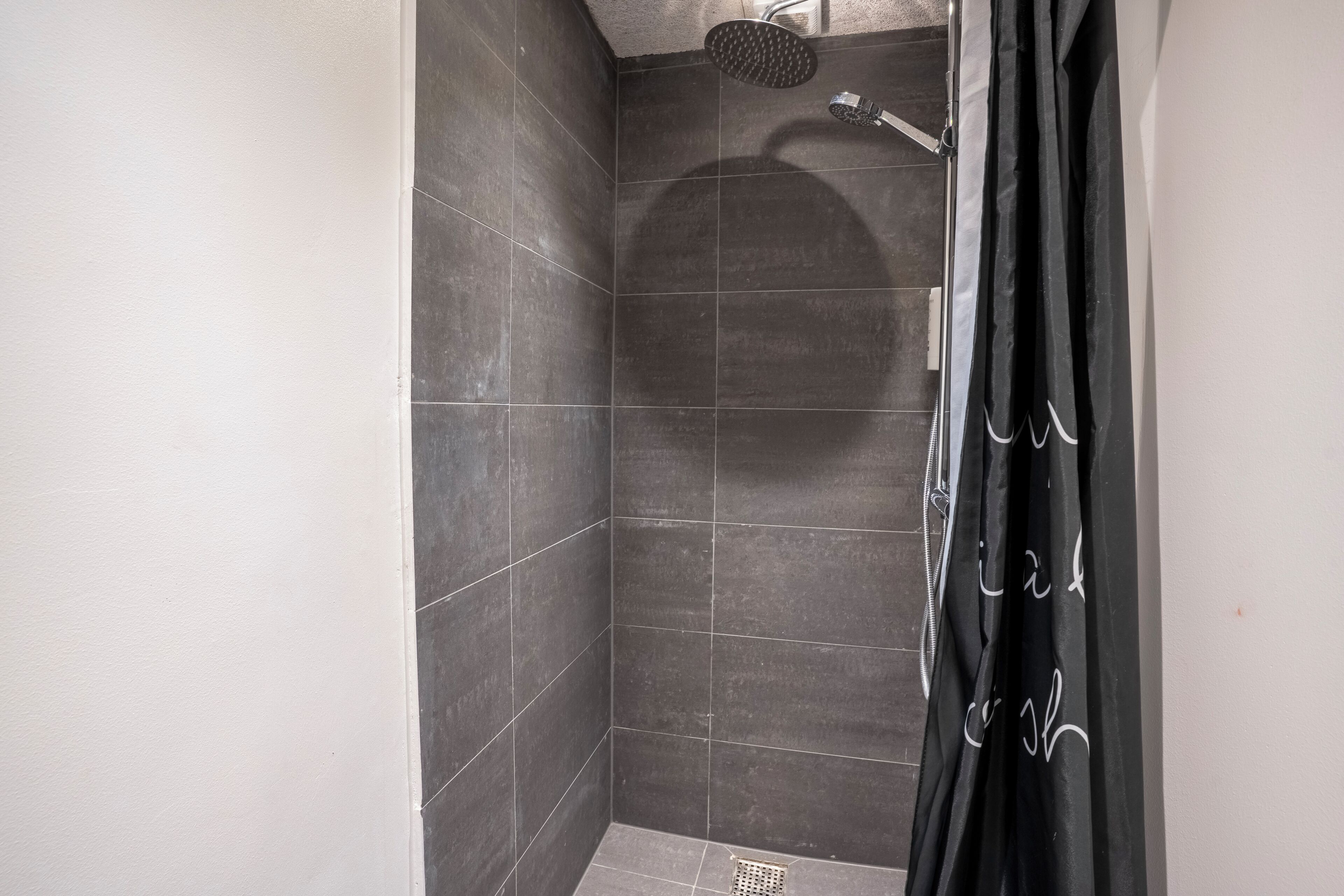 A shower area with dark tiles, a showerhead, and a black curtain.