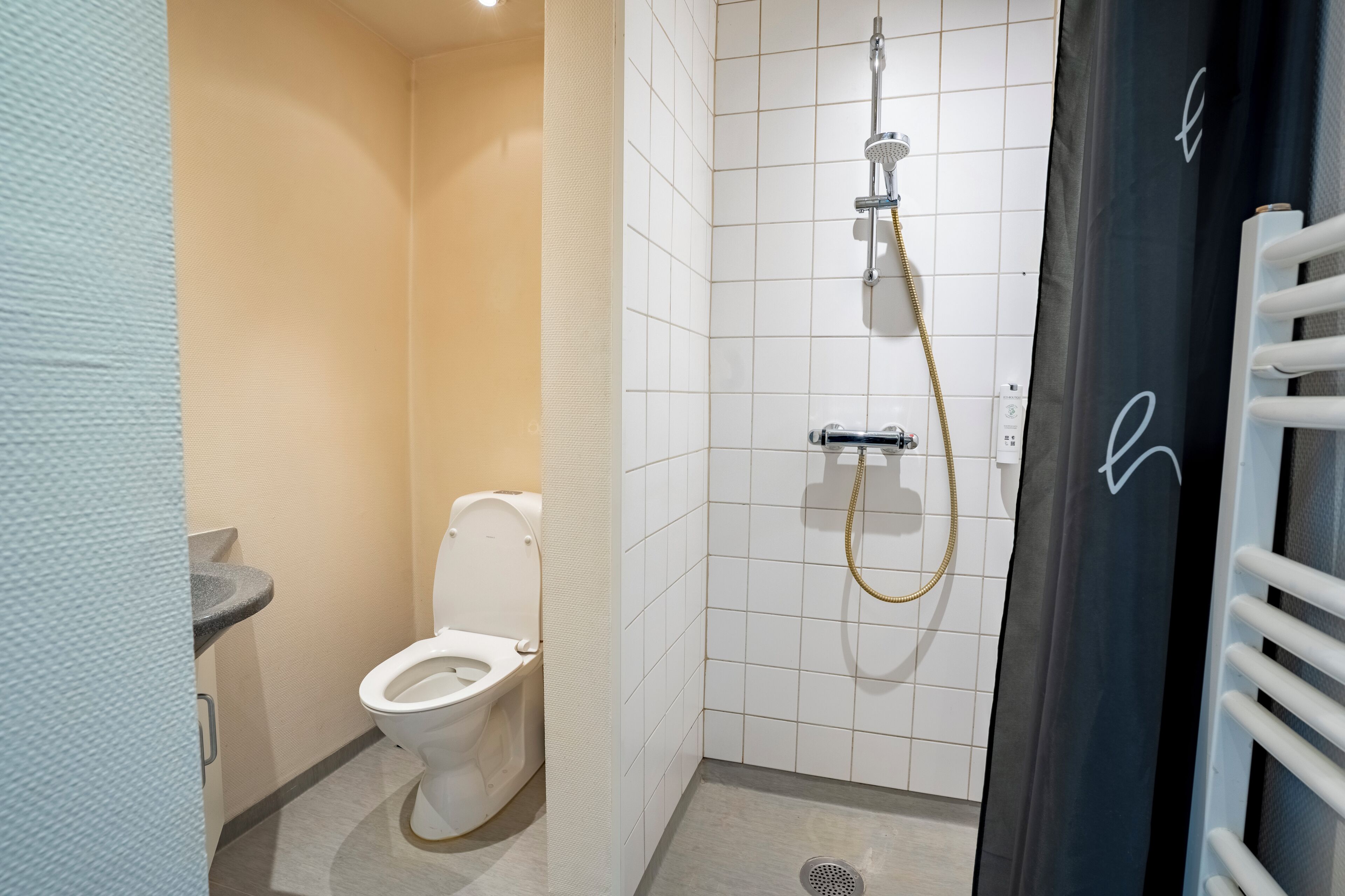 Pieni kylpyhuone, jossa on wc, suihku ja pyyheteline.