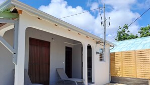 Área externa coberta com duas cadeiras de descanso, uma porta de madeira e piso de ladrilho de pedra.