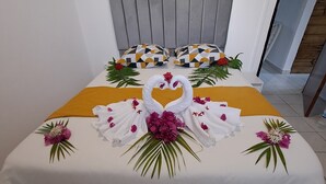 Cama bem arrumada com colcha branca, faixa amarela decorativa e almofadas de cisne.