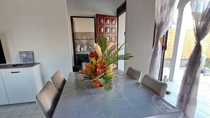 Uma área de refeições com mesa coberta, cadeiras estofadas e um arranjo floral.