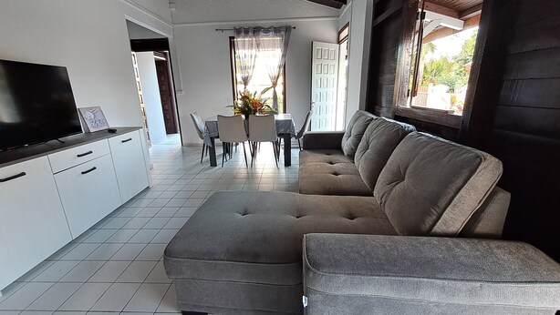 Uma sala de estar moderna com um sofá seccional, uma televisão de tela plana e uma área de jantar com mesa e cadeiras.