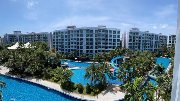 Un resort con varias piscinas, palmeras y un gran edificio de hotel al fondo.