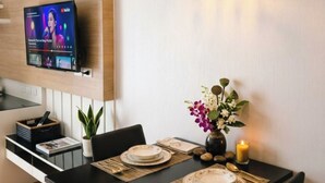 Un comedor moderno con un televisor montado en la pared, una mesa dispuesta con platos y un jarrón de flores, y una lámpara colgante arriba.
