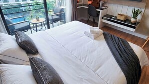 Habitación de hotel con una cama grande, un escritorio, una silla, televisión y un balcón con vistas a edificios.