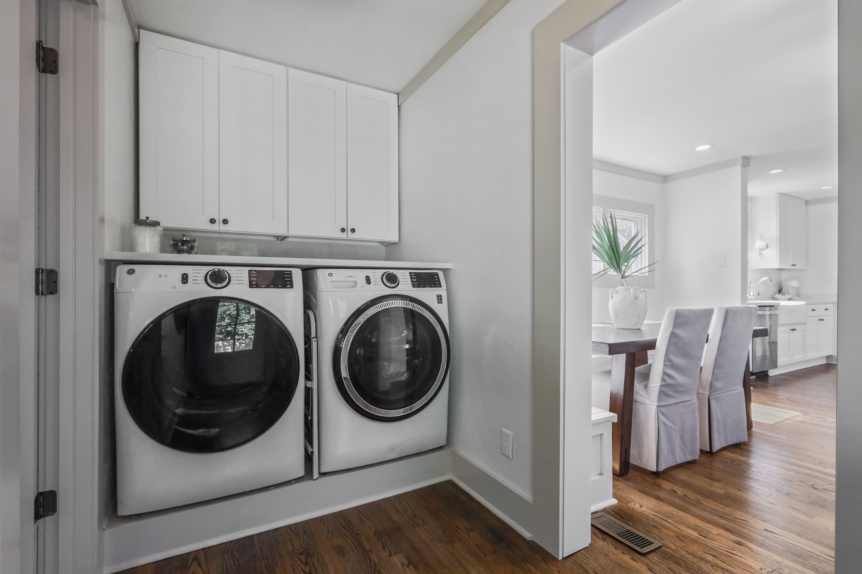 A laundry area with two front-loading washing machines, a white cabinet above, and a wooden floor.