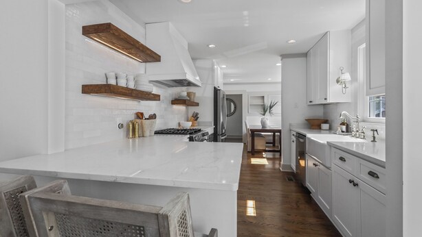 Cocina moderna con armarios blancos, una isla de mármol, estantes de madera y una isla central con estufa.
