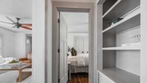 Un dormitorio moderno con suelo de madera, paredes blancas y cama con ropa de cama blanca.