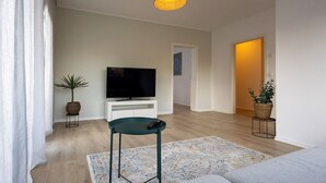 A modern living room with a flat-screen TV on a white console, a green chair, a patterned rug, and a wooden floor. - Stylish & central vacation apartment in Oranienburg (Oranienburg)