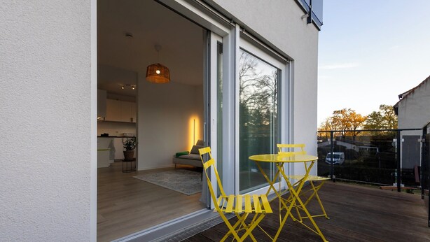 A modern outdoor patio with yellow chairs and a table, a sliding glass door leading to an interior space, and a view of trees in the background. - Stylish & central vacation apartment in Oranienburg (Oranienburg)