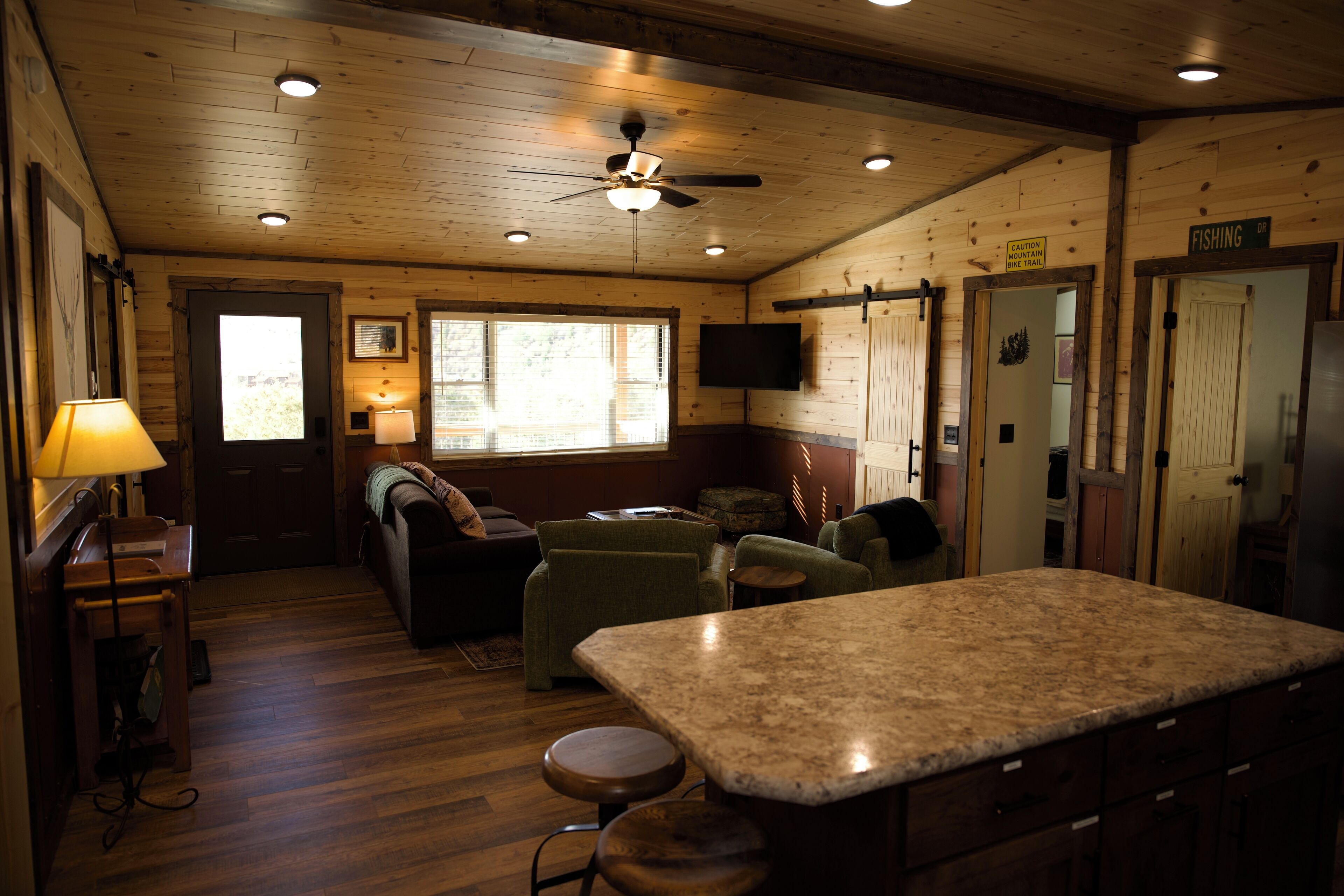 Un intérieur de chalet chaleureux avec des murs en bois, un ventilateur de plafond, un coin bar et un téléviseur.