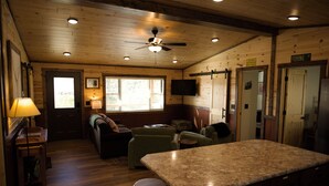 Een gezellig chaletinterieur met houten wanden, een plafondventilator, een bar en een televisietoestel.