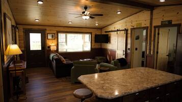 Un intérieur de chalet chaleureux avec des murs en bois, un ventilateur de plafond, un coin bar et un téléviseur.