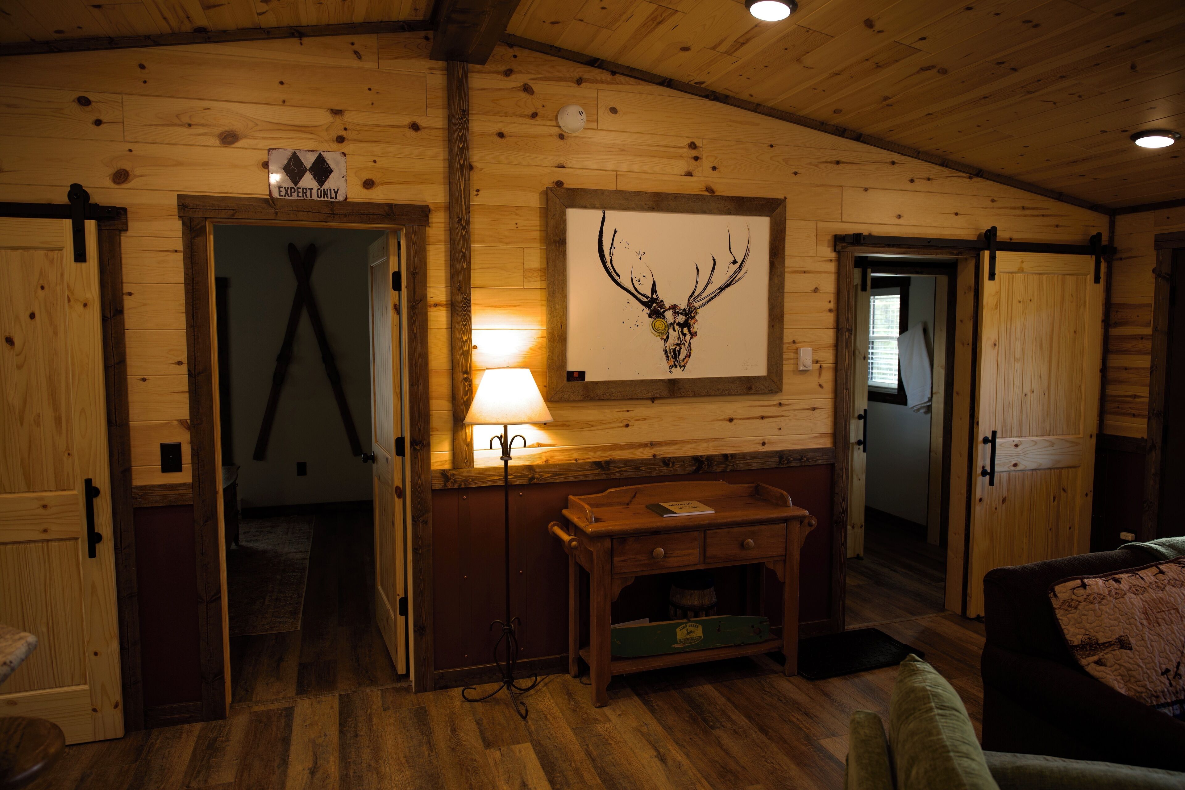 Un intérieur en bois agrémenté d’une décoration murale représentant un crâne de cerf, d’un bureau avec des tiroirs et d’une lampe.