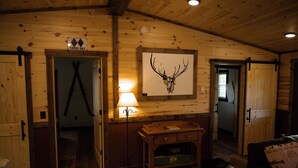 Een houten interieur met een opgehangen decoratie van een hertenschedel, een bureau met lades en een lamp.