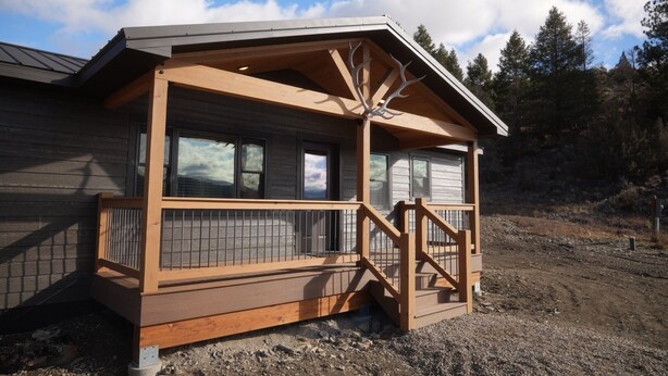 Een chalet met een houten terras, een overdekte veranda en uitzicht op het omliggende bos.