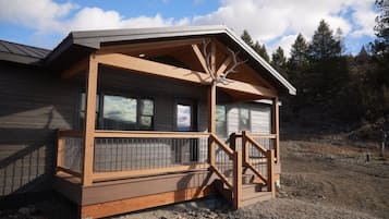 Une cabane dotée d’une terrasse en bois, d’un porche abrité et offrant une vue sur la forêt environnante.
