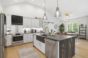 A modern kitchen with stainless steel appliances, a central island, pendant lighting, and a view of the outdoors. - Willowbrook Retreat Luxury New Build (Cromwell)