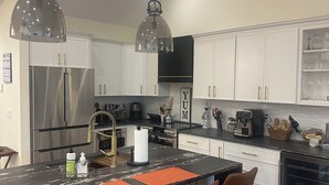 Een moderne keuken met witte kasten, roestvrijstalen apparatuur en een centraal keukenblok met barstoelen.