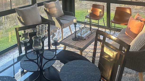 Een overdekt terras met een glazen tafel, stoelen en een plafondventilator.