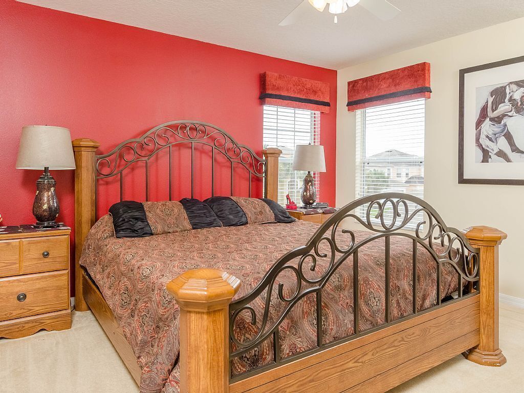 A bedroom with a red wall, a wooden bed frame, and two bedside tables with lamps.