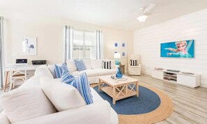 Ein modernes Wohnzimmer mit einem weißen Sofa, blauen und weißen Kissen, einem Couchtisch und einem Fernseher an der Wand.