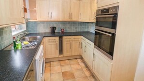 A kitchen with wooden cabinets, a black countertop, a double oven, and a washing machine. - Luxe Leamington Spa Retreat (Royal Leamington Spa)