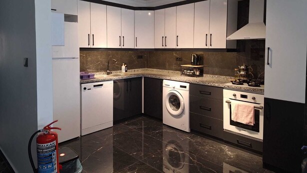 A modern kitchen with white cabinets, a built-in washing machine, a stove, and a fire extinguisher.