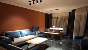 A modern living room with a sofa, armchairs, a coffee table, a dining table with chairs, and a chandelier.