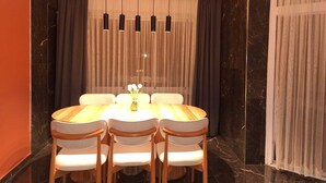 A dining area with a round table, four chairs, a chandelier, and a curtain backdrop.