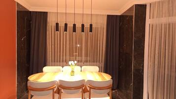 Un espace repas comprenant une table ronde, quatre chaises, un lustre et un rideau en fond.