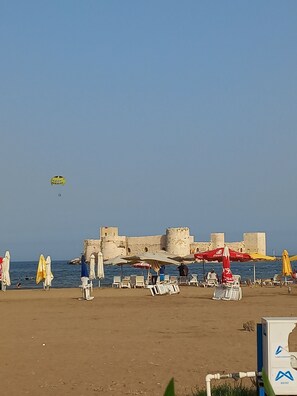 Una playa con sombrillas, sillas y una estructura parecida a un castillo al fondo.