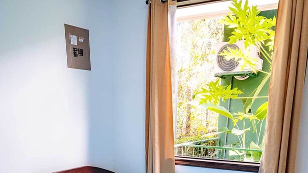 Ein Einzelbett mit blauer Matratze in einem Zimmer, das ein Fenster, eine Wand-Klimaanlage und einen gefliesten Boden hat.