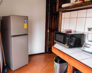 Une cuisine compacte équipée d’un réfrigérateur en acier inoxydable, d’un four à micro-ondes et d’un mixeur, le tout posé sur un plan de travail en bois.