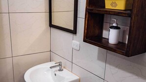 Ein Badezimmer mit einem weißen Waschbecken, einer Toilette und einem Spiegel über dem Waschbecken. Ein Regal mit einem gelben Korb und einer weißen Flasche.