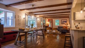 Una cocina amplia con vigas de madera, un comedor con sillas traslúcidas y una sala de estar con sofá y mesa de centro.