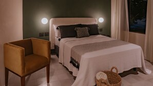 A bedroom with a bed, a chair, a nightstand, a wall-mounted lamp, and a window with curtains.