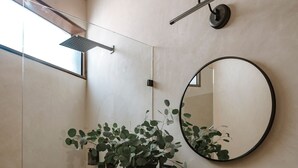 A modern bathroom with a black marble sink, a round mirror, a potted plant, and a glass shower enclosure.