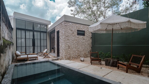 A modern outdoor pool area with stone walls, lounge chairs, and a large umbrella.