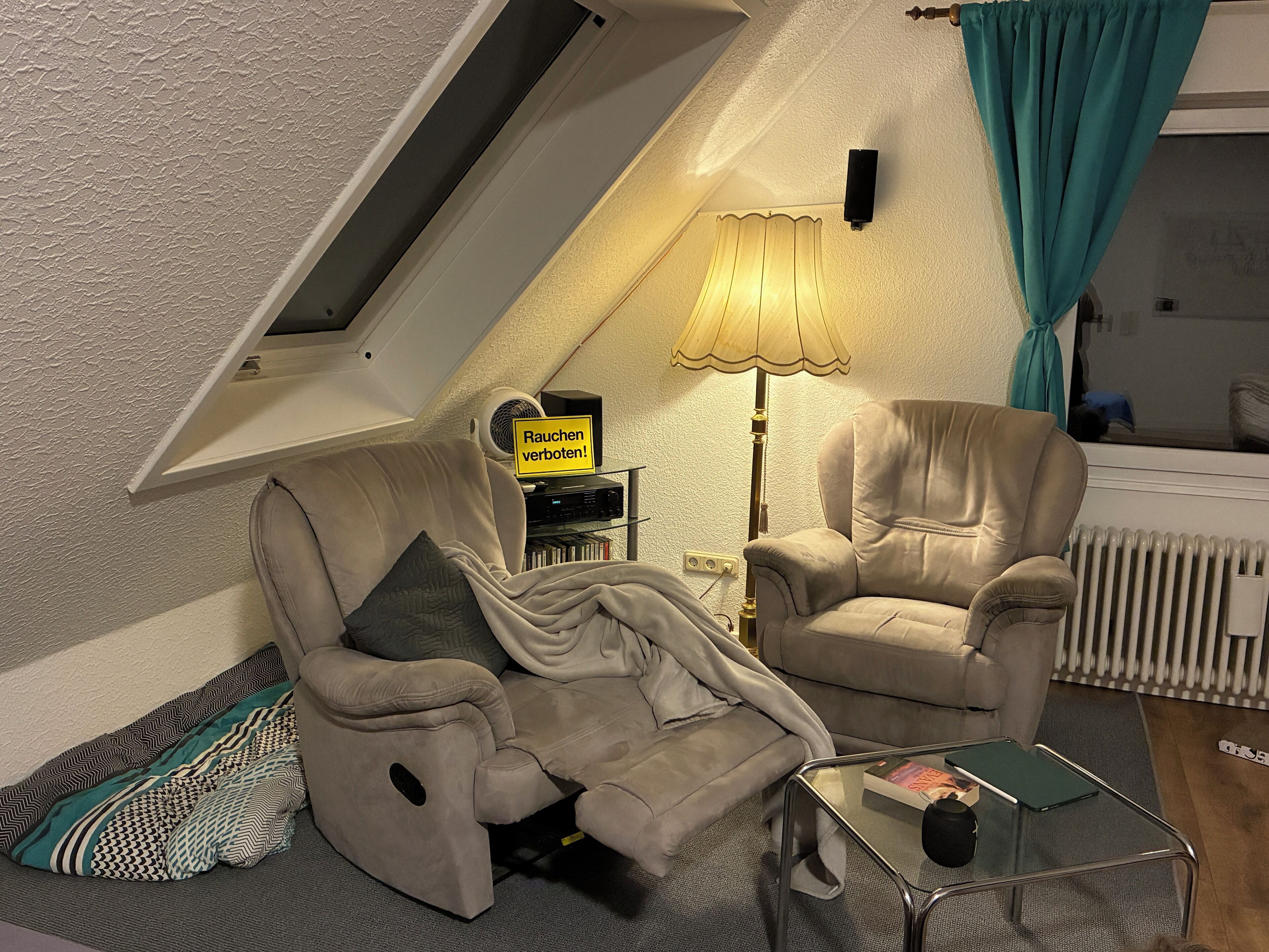 A cozy living room with a recliner, a glass coffee table, a lamp, and a sign that reads "Rauchen verboten!" (Smoking prohibited!).