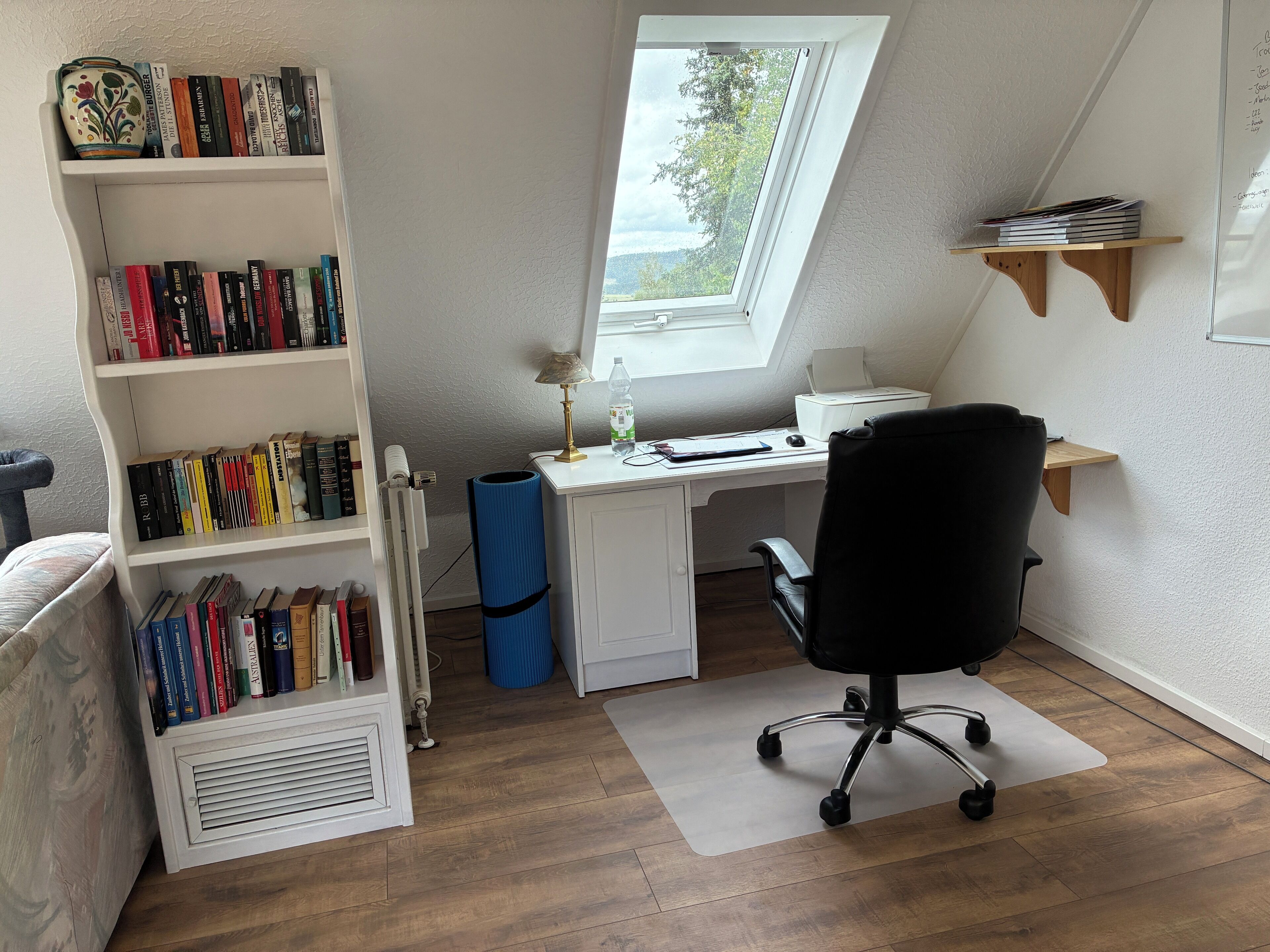 A home office with a desk, chair, bookshelf, and a window with a view.