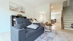 A modern living room with a grey sofa, a remote control, a patterned throw, and a painting on the wall. - Cozy Home + Free Parking (Winston-Salem)