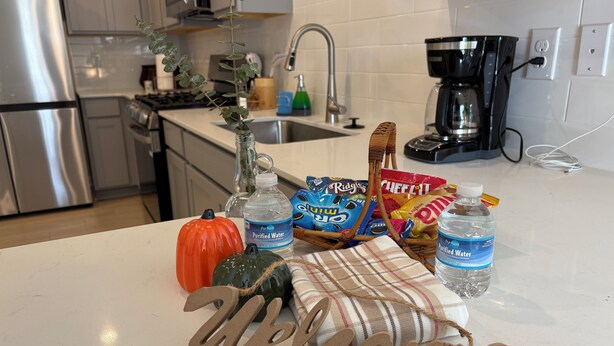 A kitchen counter with a 'Welcome' sign, a water bottle, snacks, a pumpkin, and a vase with a plant. - Cozy Home + Free Parking (Winston-Salem)