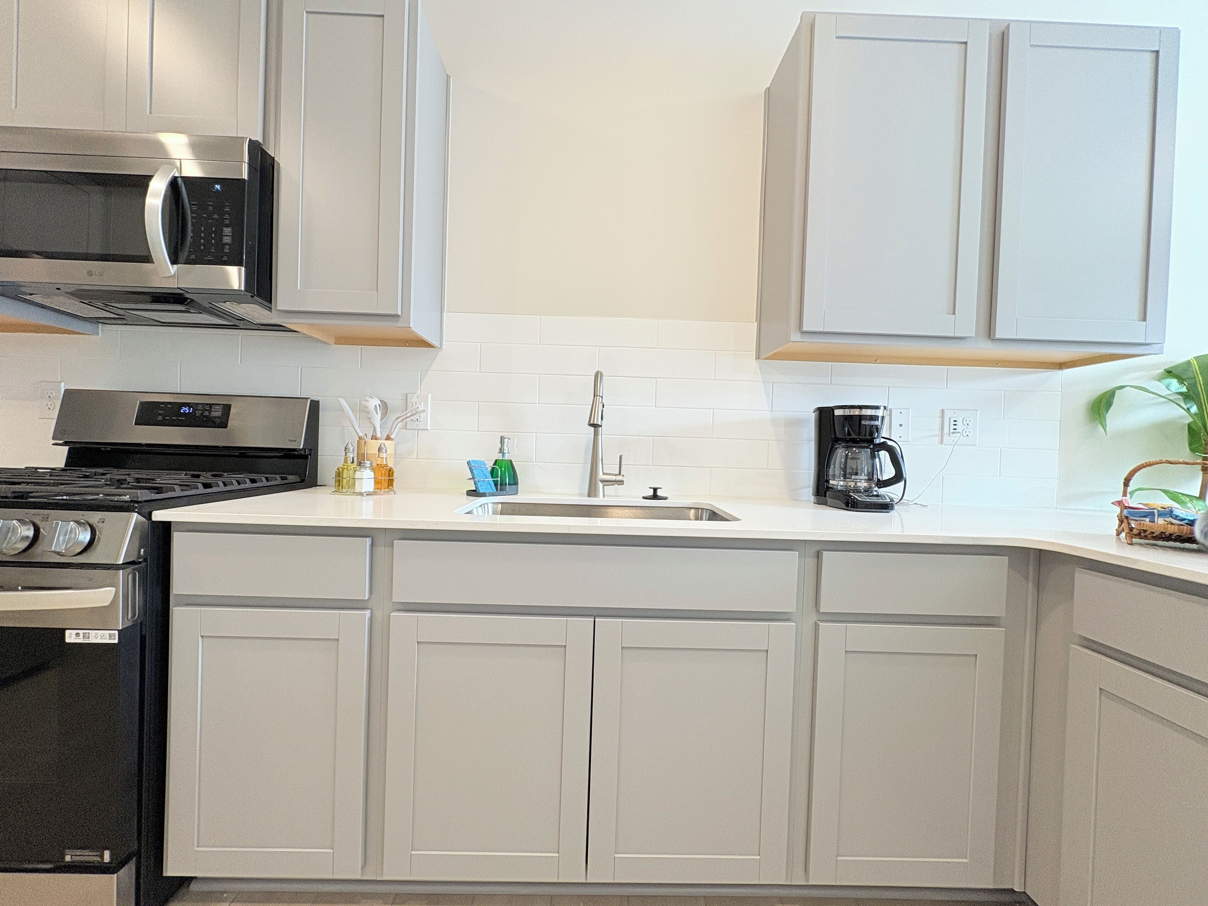 A modern kitchen with white cabinetry, a stainless steel microwave, a stove, a sink, and a coffee maker.