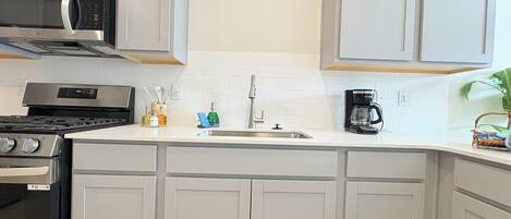 A modern kitchen with white cabinetry, a stainless steel microwave, a stove, a sink, and a coffee maker.