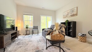 A living room with a TV, two windows, a sofa, a chair, a coffee table, and a bookshelf. - Cozy Home + Free Parking (Winston-Salem)