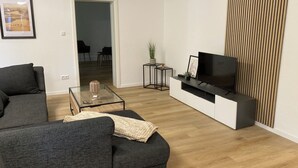 A modern living room with a grey sofa, a glass coffee table, a TV on a white entertainment unit, and a wooden floor. - Vacation apartment Dorfliebe Minden by Engelmann (Minden)
