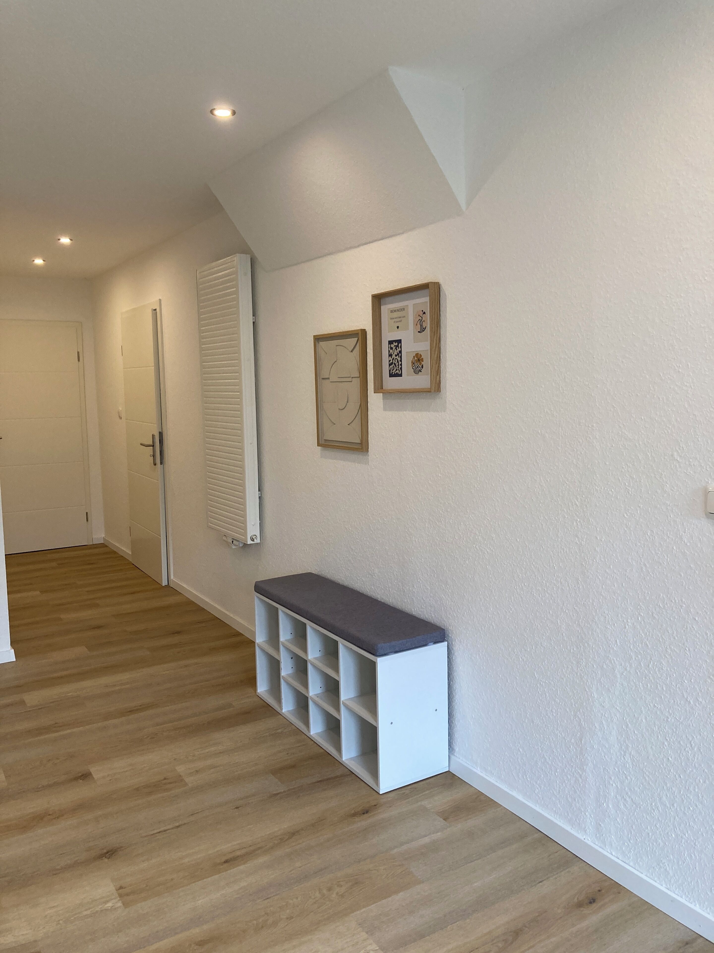 A hallway with a bench, a door, and two framed artworks on the wall.