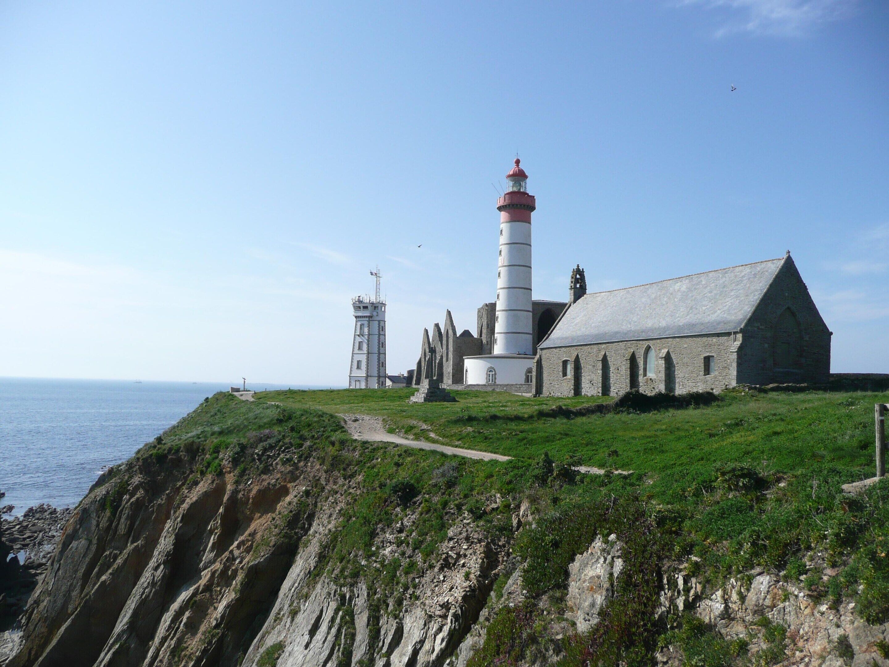A coastal lighthouse and adjacent stone building with a clear path leading to the entrance.